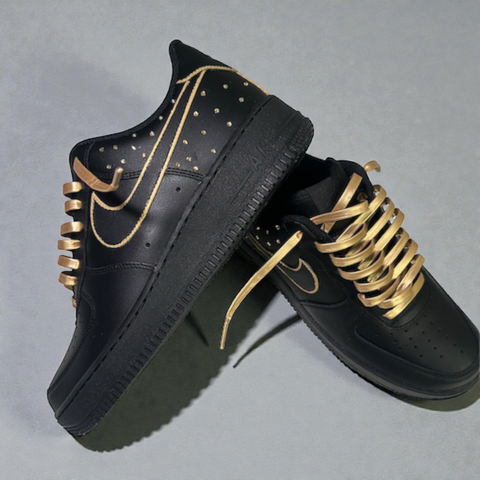 Two custom Black Nike Air Force 1s stacked one on top of the other, highlighting the side-panel gold Swarovski crystal detailing and leather lacing.