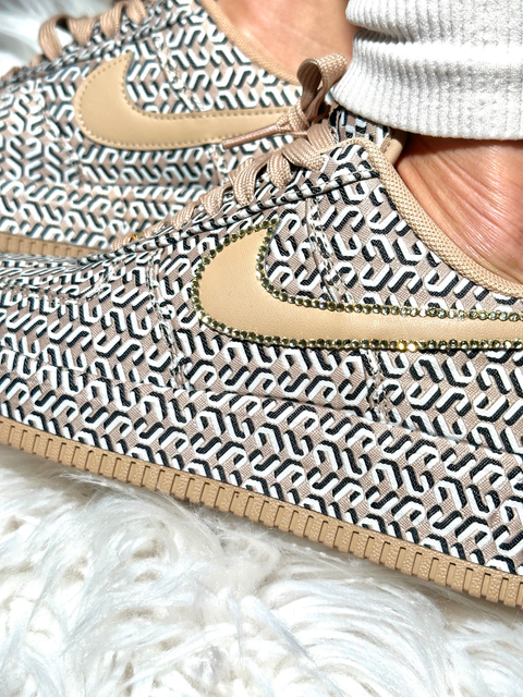 A pair of custom Nike Air Force 1 sneakers featuring tan laces, gold lace locks, and Swarovski crystal accents