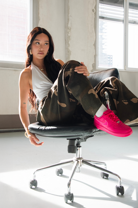 Lifestyle shot of a model wearing custom fuchsia Nike Air Force 1 sneakers with Swarovski accents and camo trousers