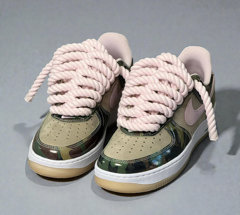 Top-down studio shot of Camo AF1s on a neutral background, showcasing the 1.0 rope lace conversion in pastel pink.